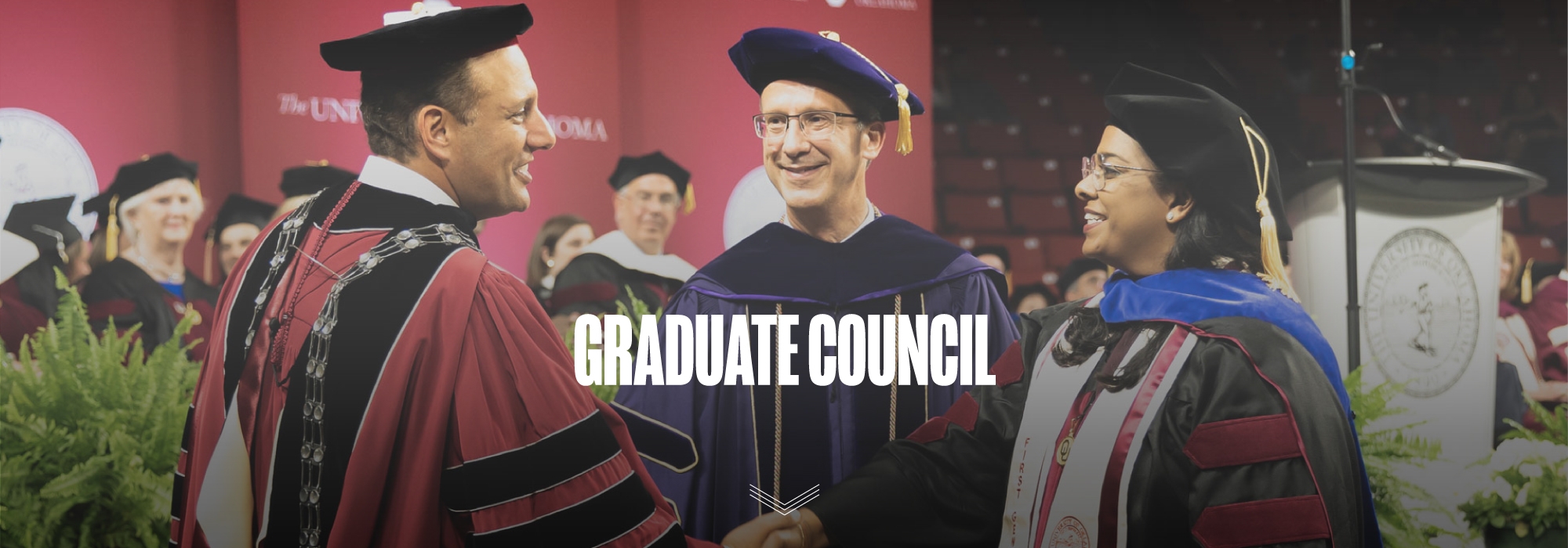 Dean hewes standing beside president harroz shaking the hand of a recent doctoral graduate