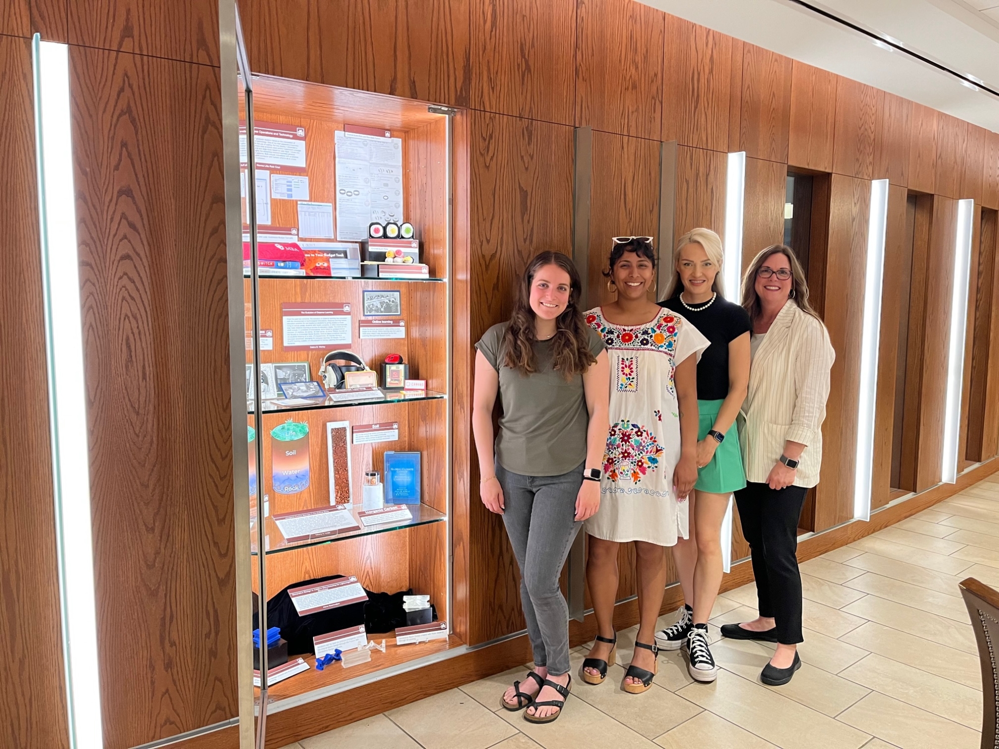 Four people stand next to a library shelf display of items.