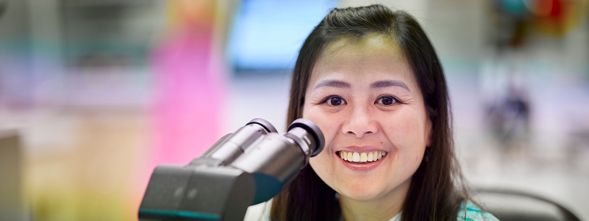 Lab technician smiling while looking up from microscope