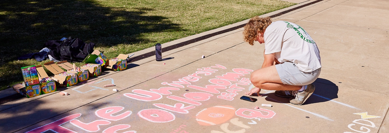 student using chalk to draw on the south oval sidewalk for homecoming.