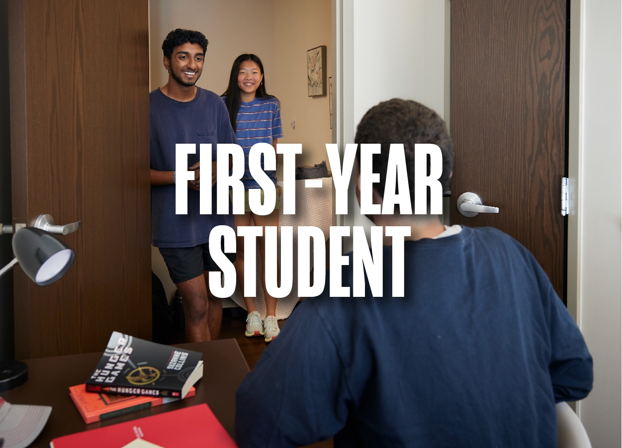 Two students stand in the doorway of a Cross Village room talking to another student sitting at a desk.