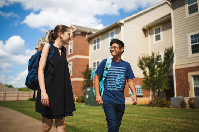 One female and one male student walking outside of Traditions Square Apartments.