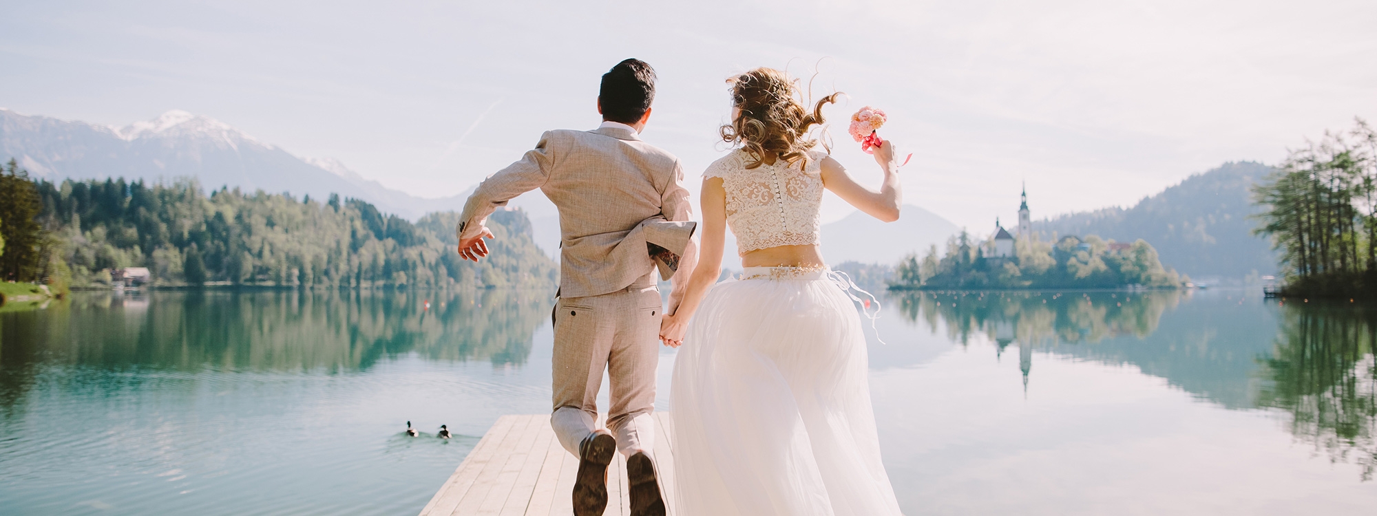 Married couple jumping on a pier facing away from the camera.
