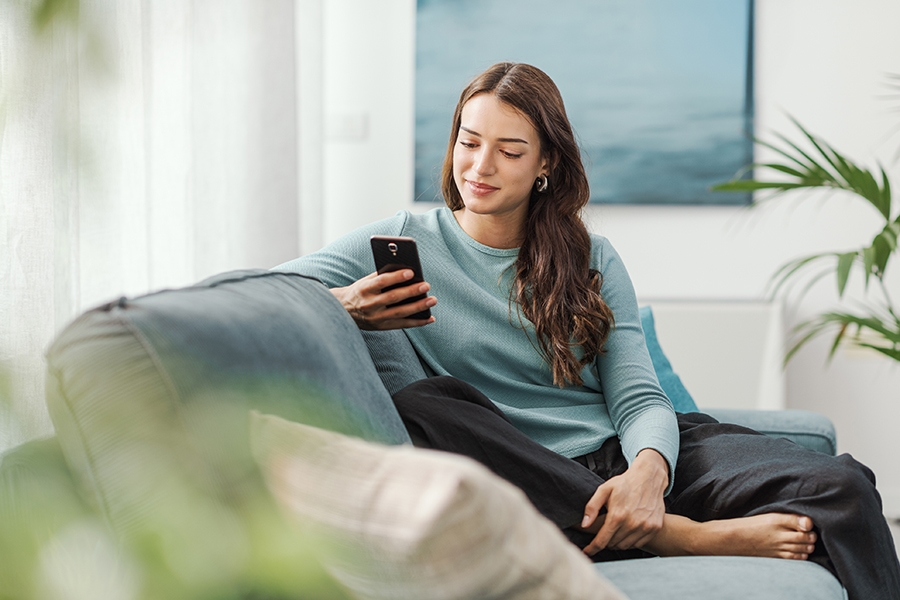 Woman sitting on her couch using a phone.