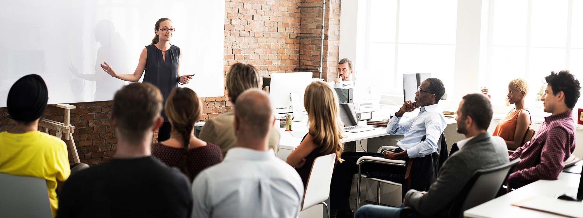 Woman teaching a class of continuing professionals in a modern office building classroom.