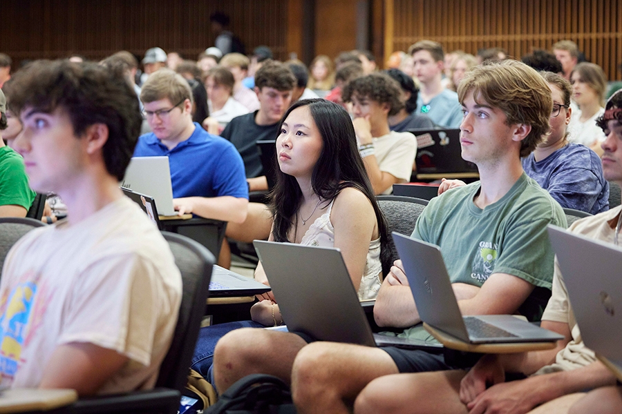 Students with laptops sitting in an auditorium.