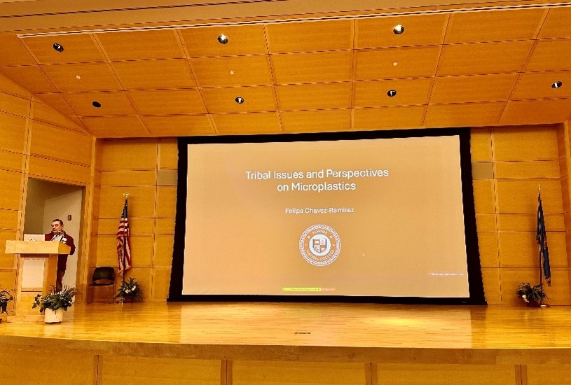 Speaker on a stage with a presentation title screen in the background