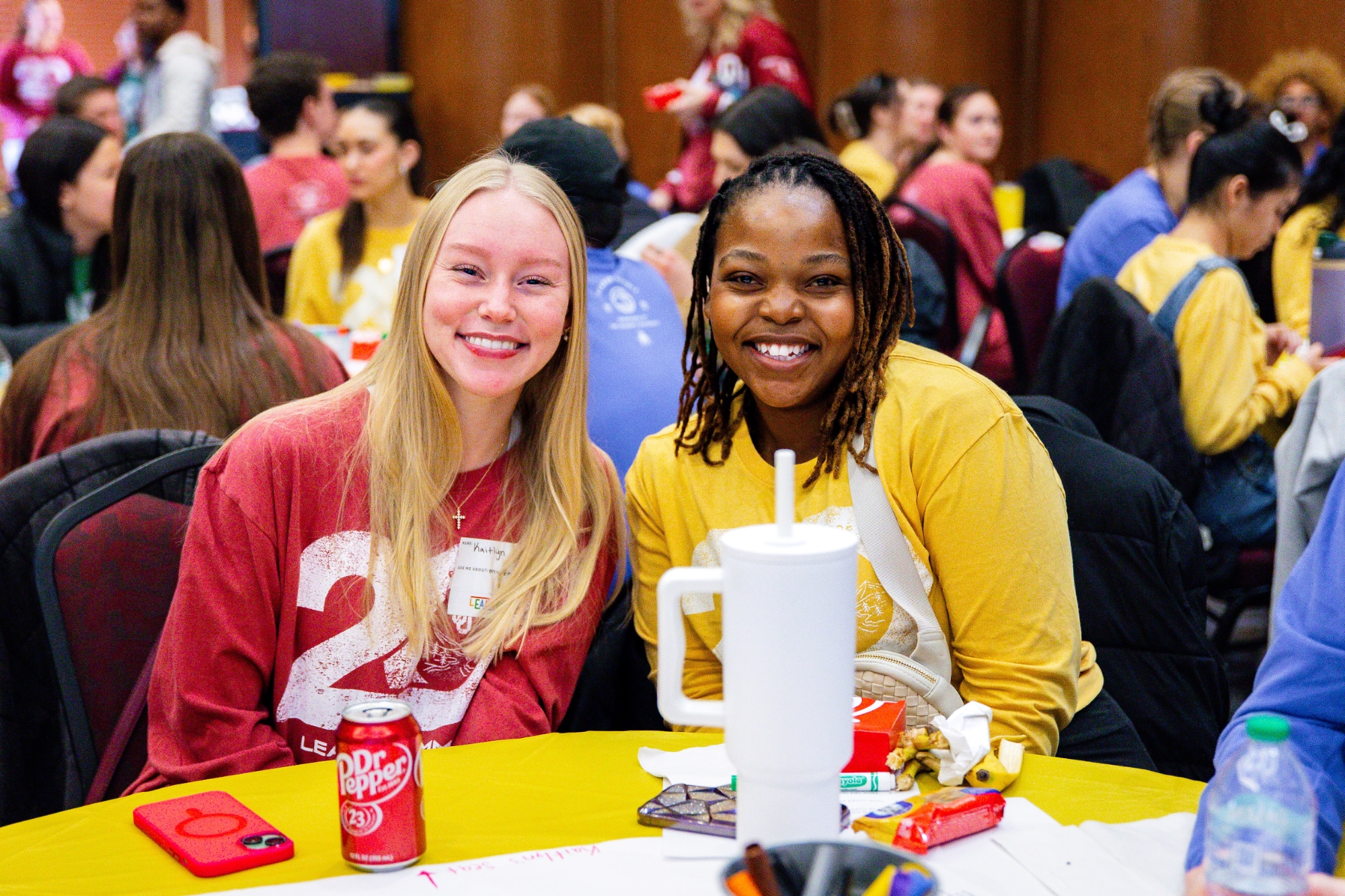 Two students sitting at a table and smiling at the 2025 Leader Summit.