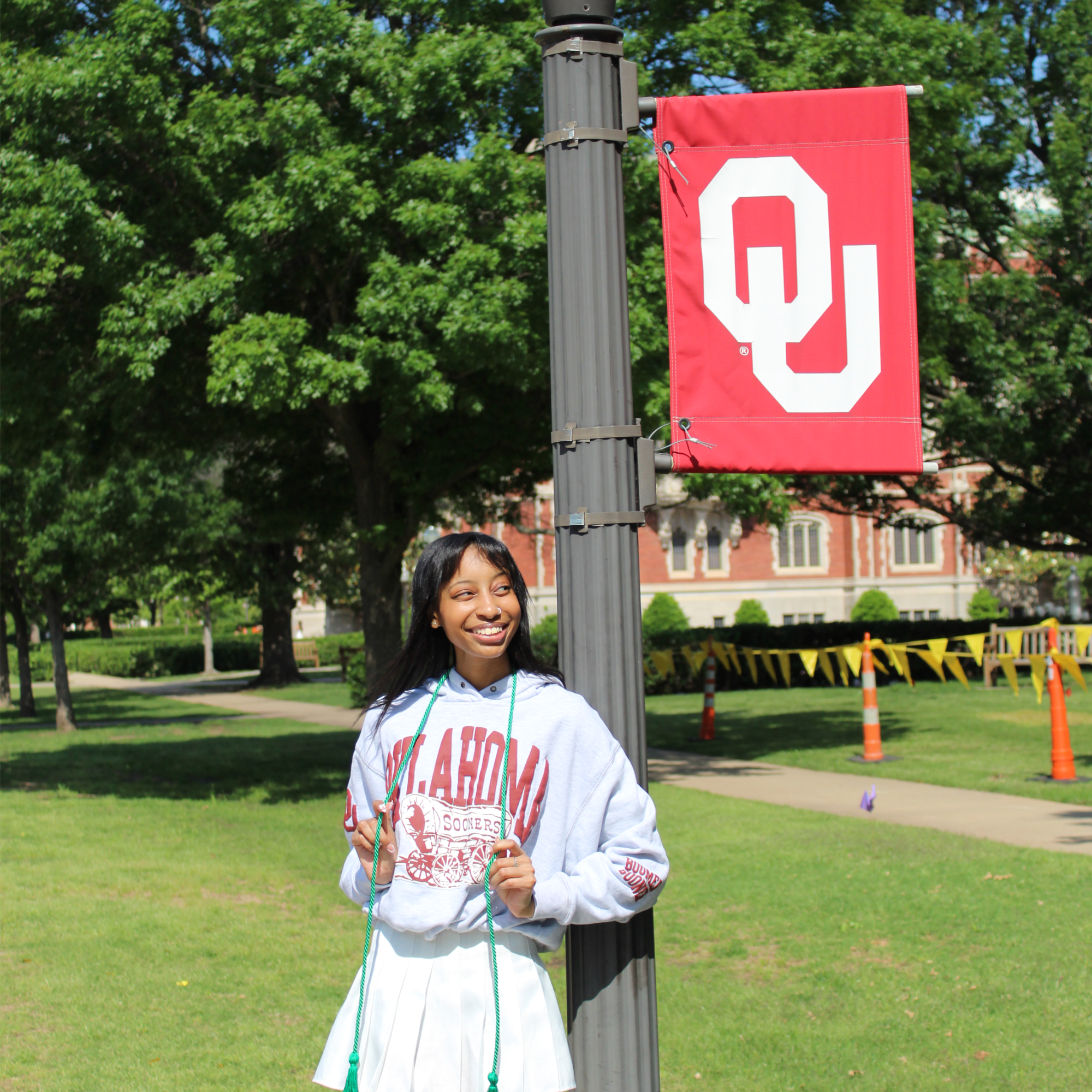 An OU student standing next to an OU light post banner with a green cord representing their Standard Award achievements. 