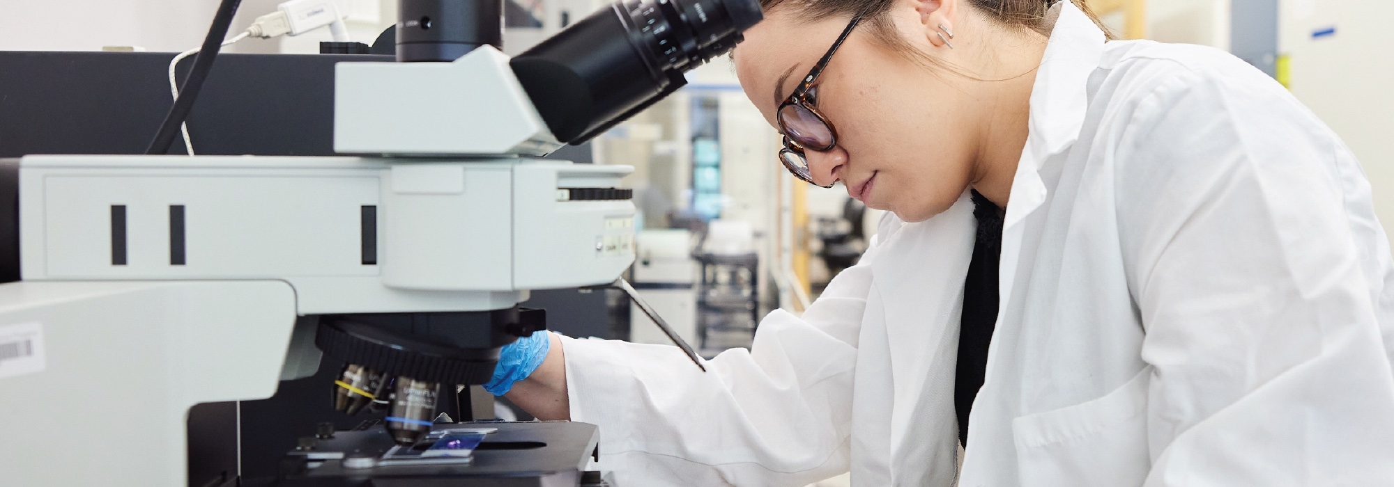 A researcher in a white lab coat working with a microscope.