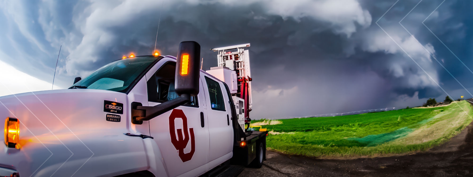 An O U radar truck in front of a large thunderstorm, surrounded by fields.
