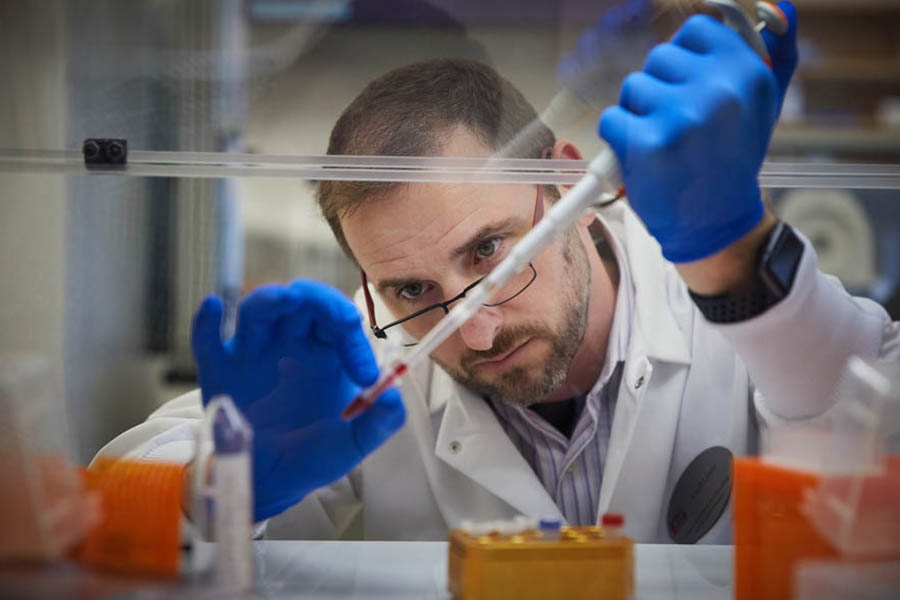 A research wearing gloves, using a pipette to fill a syringe.