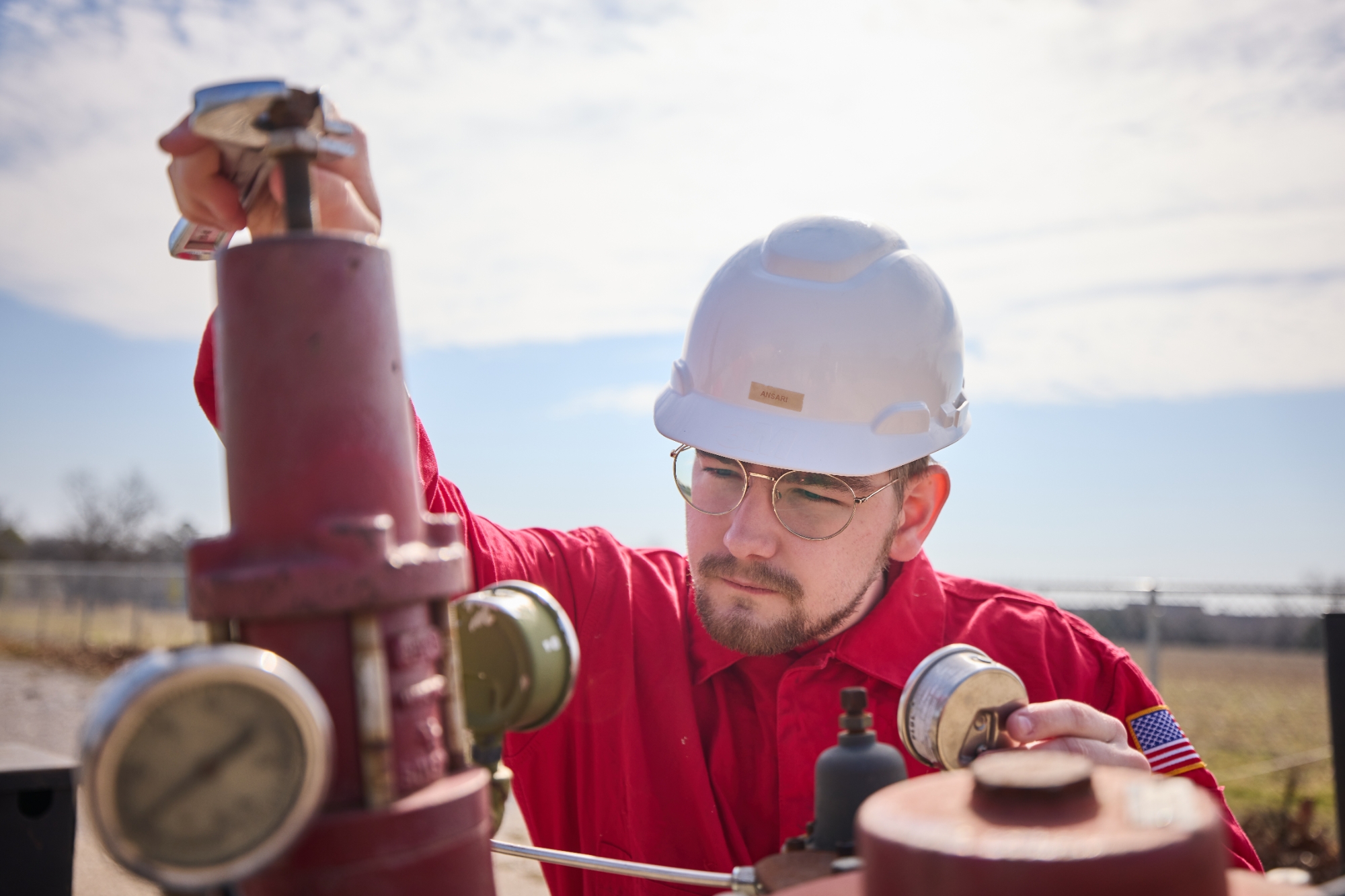 A person in a hardhat, adjusting a pipe with a wrench.