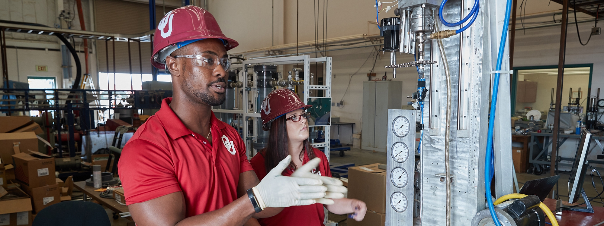 Two O U students in hard hats, working with machinery.