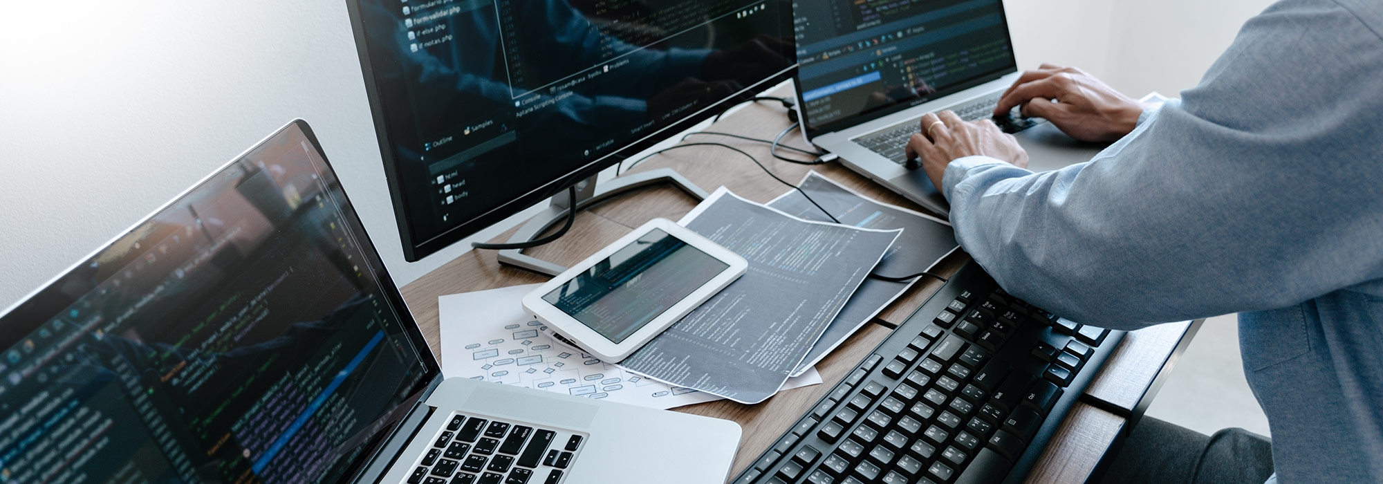 Programmer typing code on laptop computer while using multiple screens for testing views.