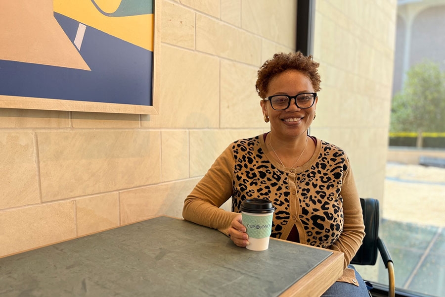 Lisa Campbell sitting at a bistro table with a to-go cup of coffee.