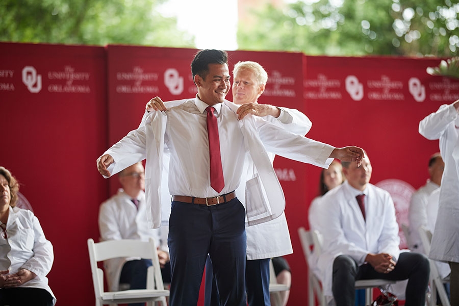 A student extends his arms to receive his white coat.