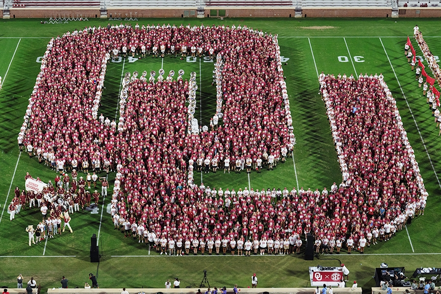 The Class of 2028 stands together in the center of a football field in the shape of the intelocked letters O and U..