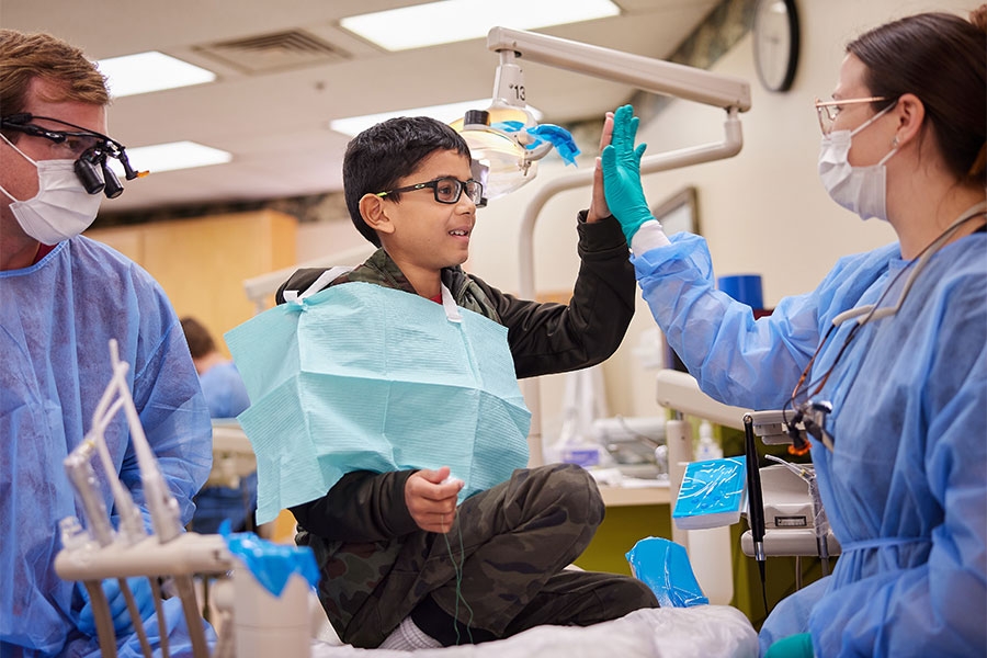 Two dentists work together with a young patient. 