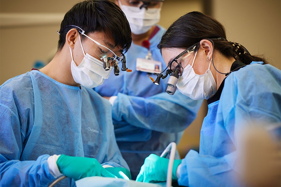 Two dentists working on a patient while another supervises. 