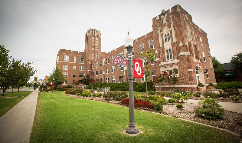 A decorative brick building on campus with a lamp post with OU and Campus Corner flags attached.