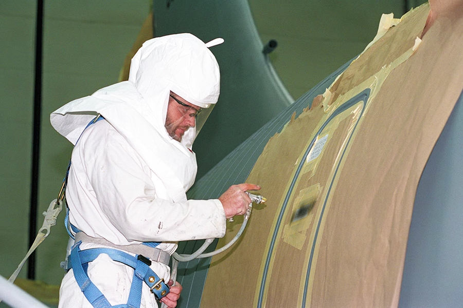 A man wearing protective gear painting a military plane.