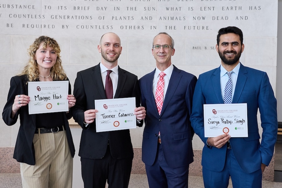 Four people stand in a line, with the three students holding up certificates.