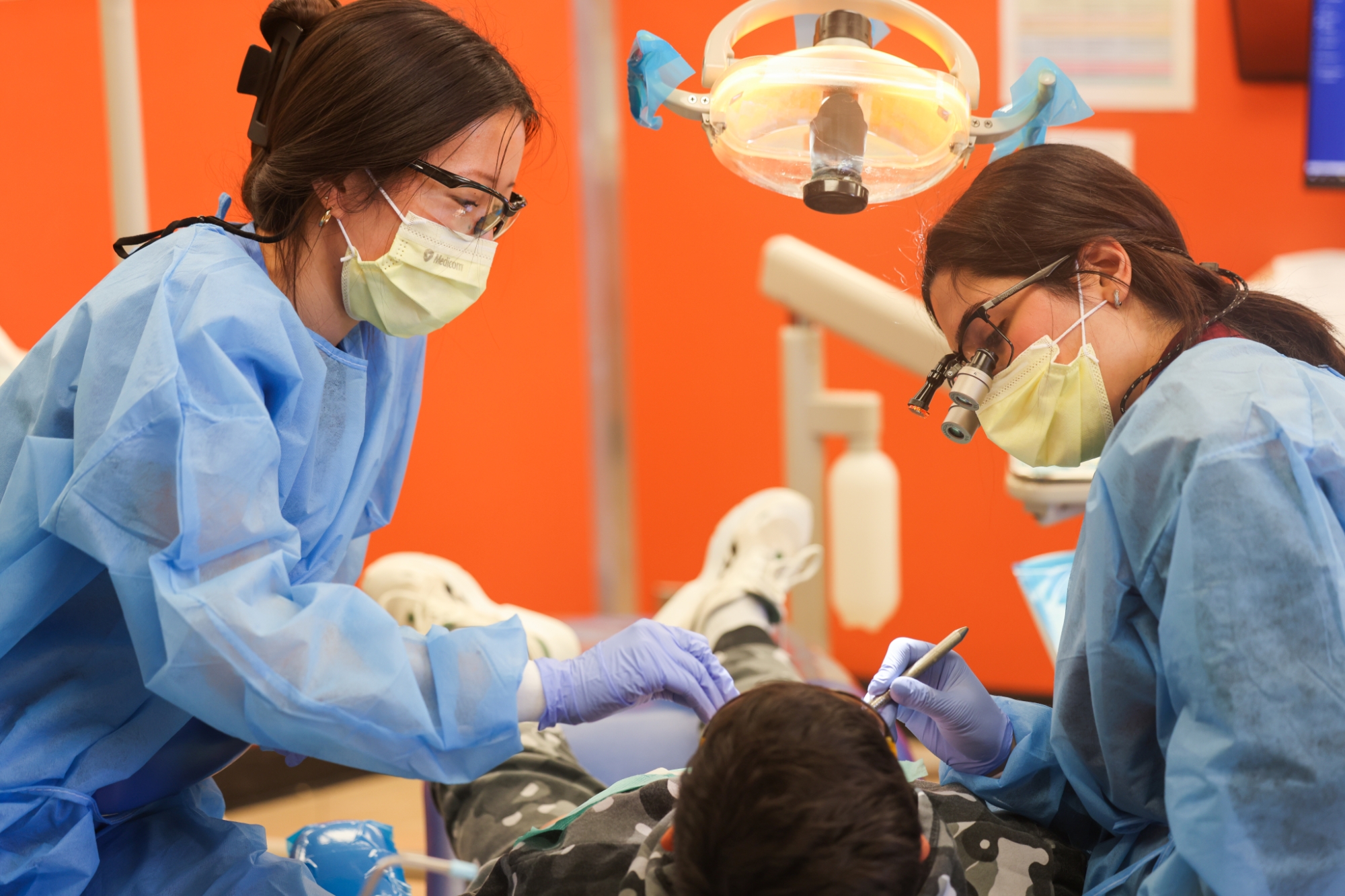 Two dental students stand over a child receiving dental care.