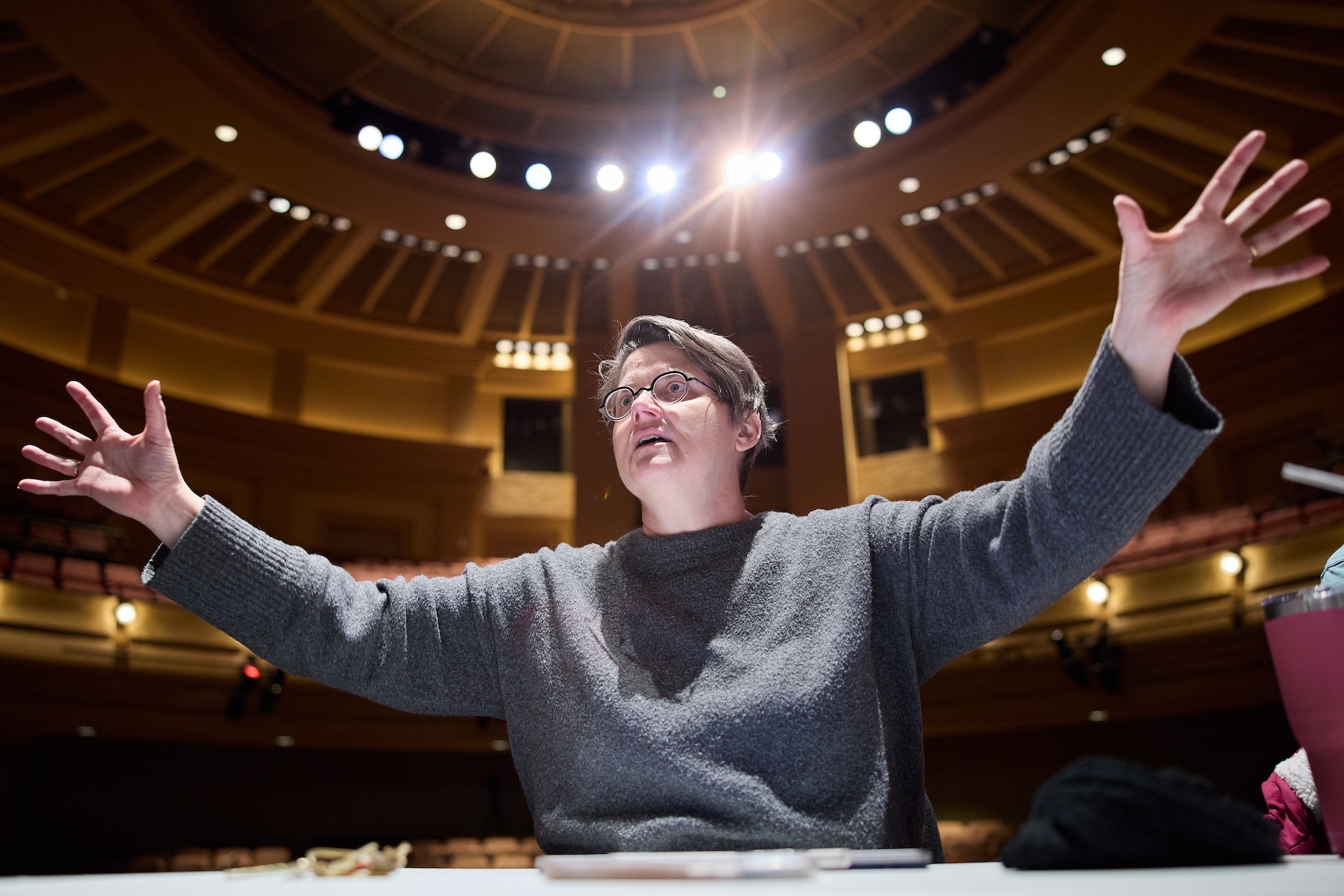Nicole Kenley-Miller with her arms spread wide, an auditorium behind her.