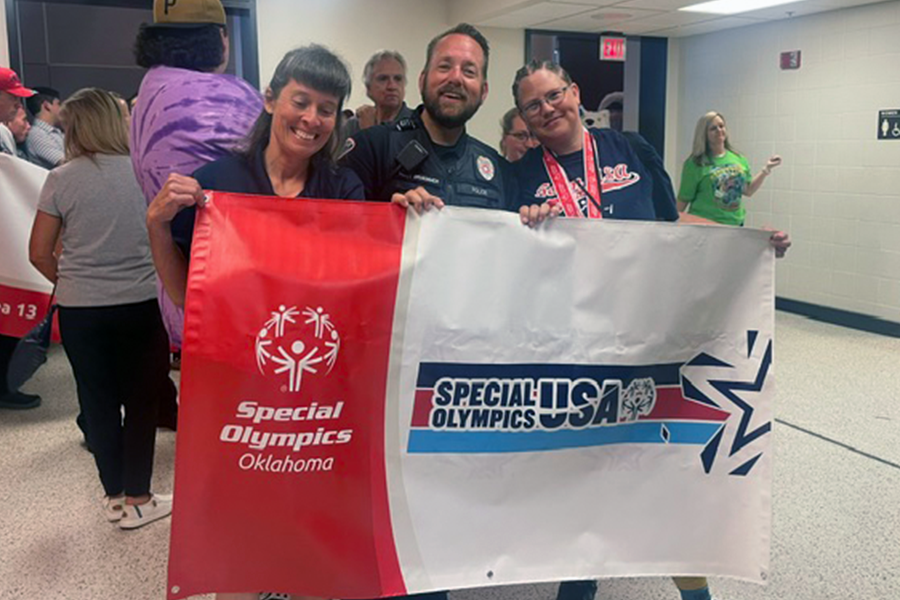 Bobby stands with two others behind a flag for the Special Olympics.
