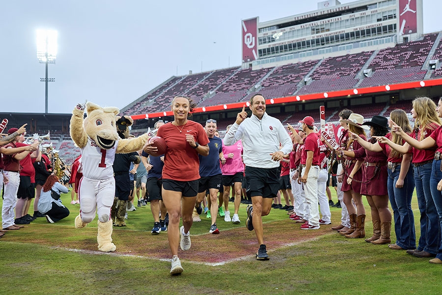 Photo of a group of people running in a stadium with crowd surrounding them.