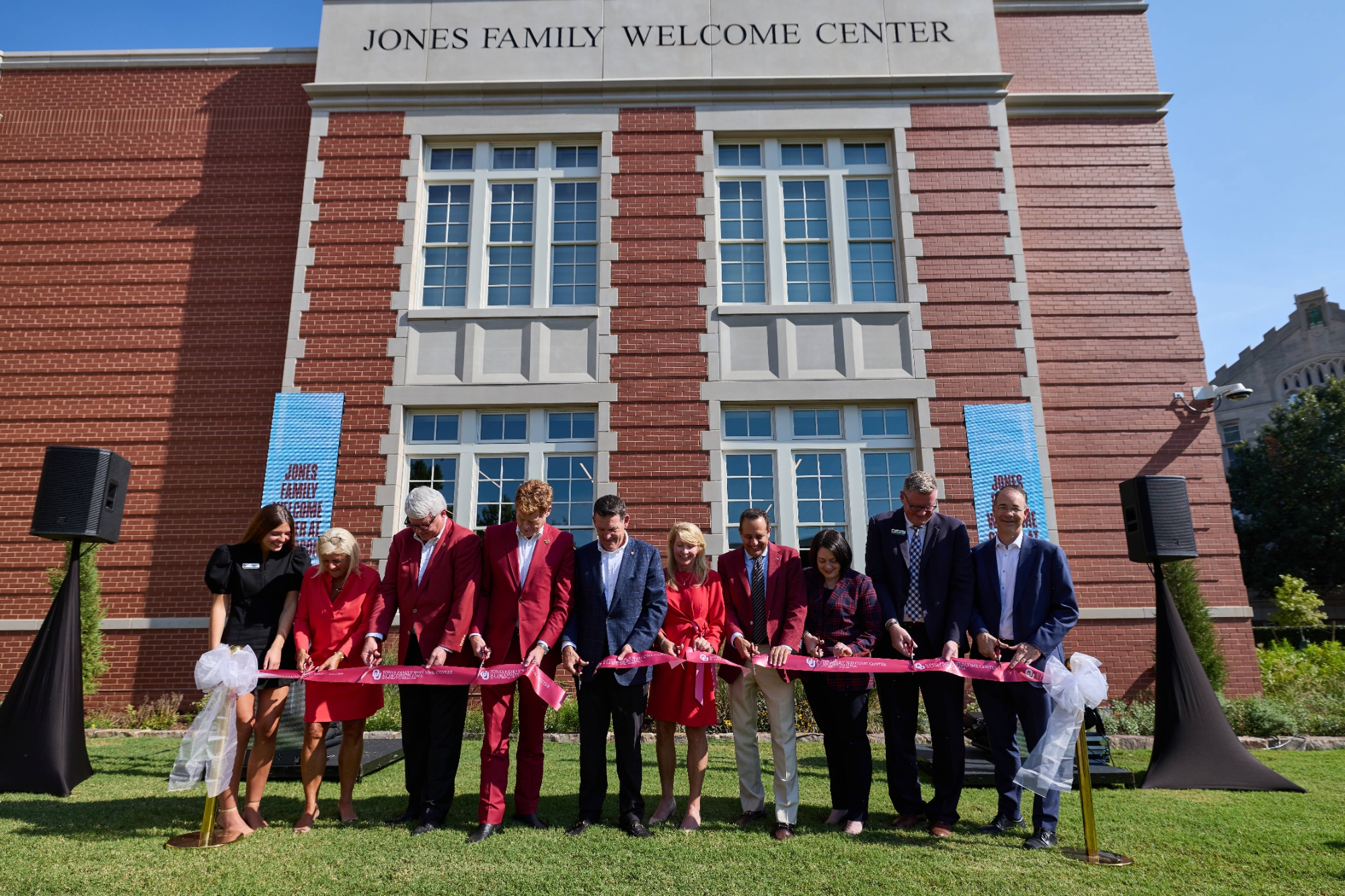 A row of 10 people cut a ceremonial ribbon outside a building inscribed "Jones Family Welcome Center."