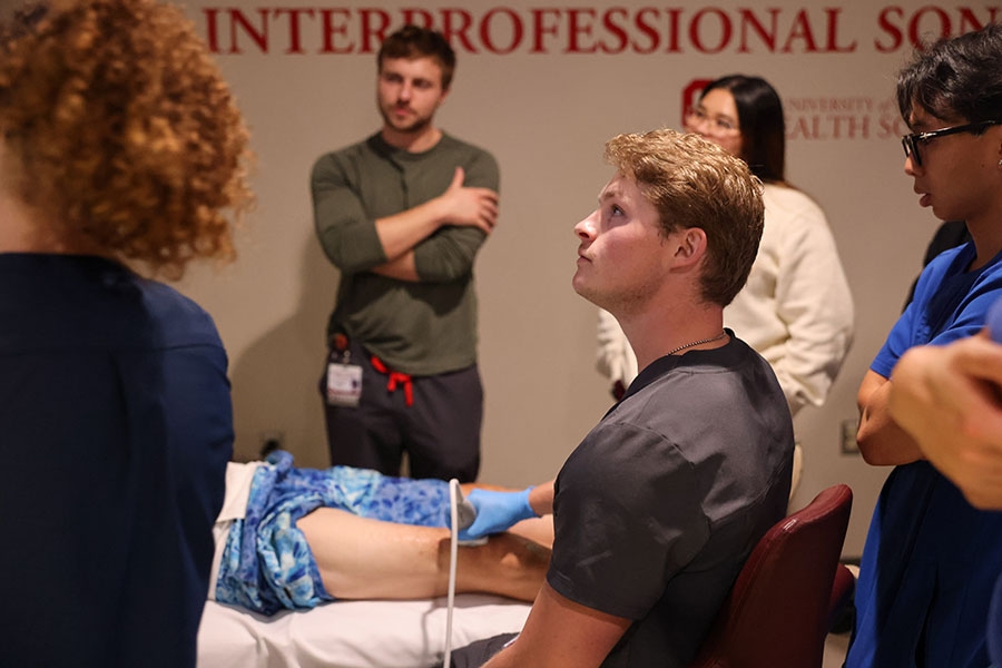A man in plainclothes uses an ultrasound transducer on a patient's leg.