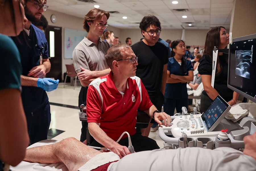A man in a University of Oklahoma polo shirt uses an ultrasound transducer on a patient while looking at the scanned image on a computer.