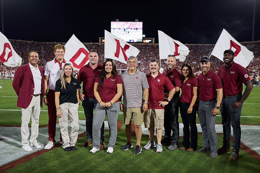 A group of adults stand together on a football field during a night game.