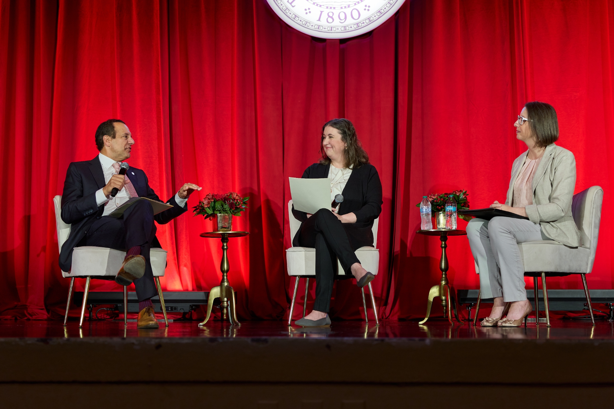 Three people sitting on chairs on a stage.