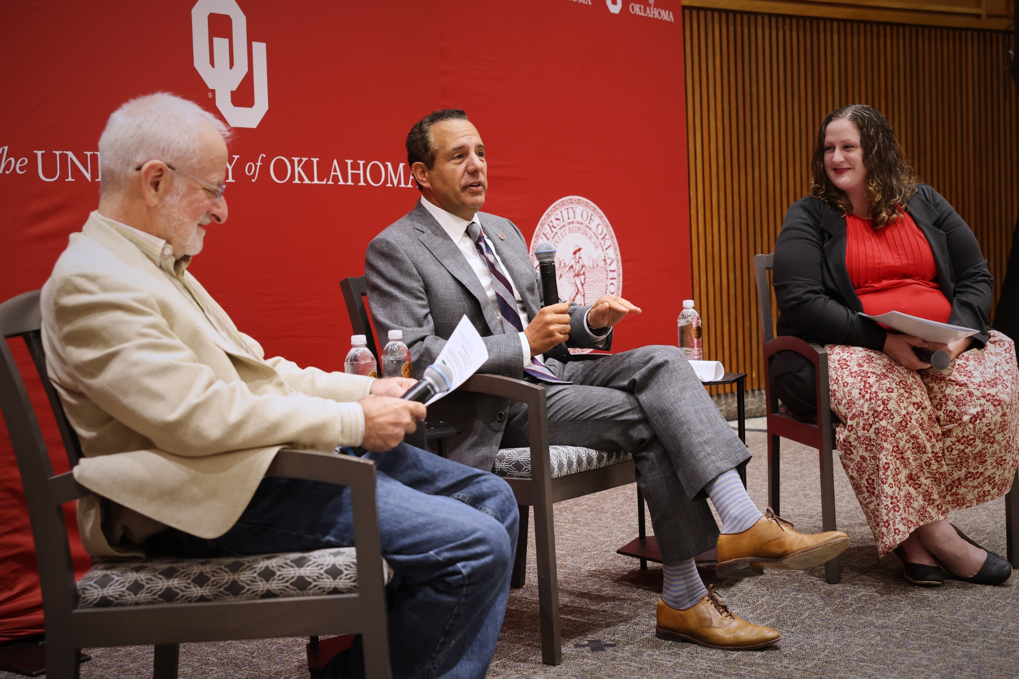 Three people sitting on chairs on a stage.
