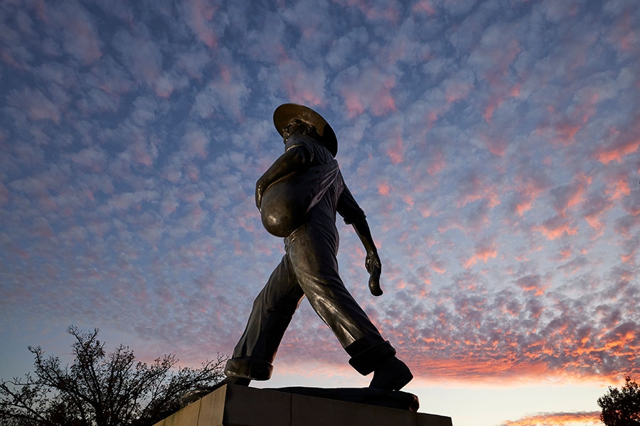 The OU Seed Sower statue captured at a low angle. The background in a sunset full of small clouds.