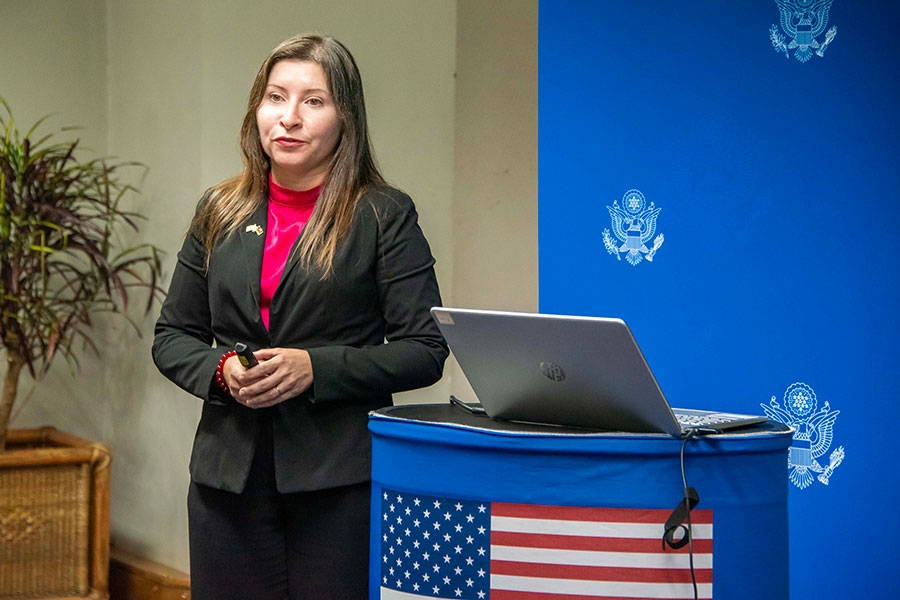 A woman stands next to a podium with an American flag during a presentation.