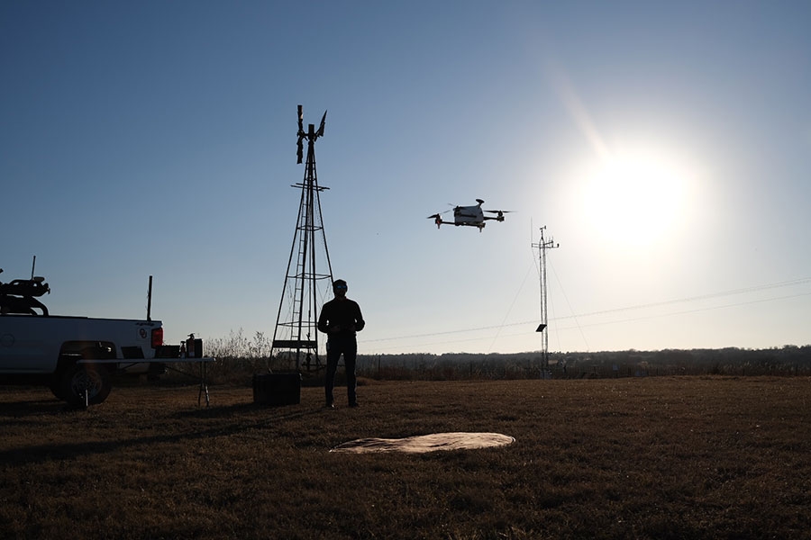 A man pilots a drone flying above a field.