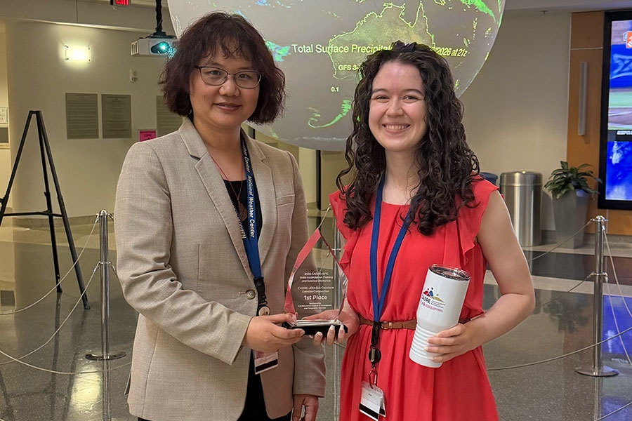 Two women standing together. The one on the left hands a glass award to the one on the right.
