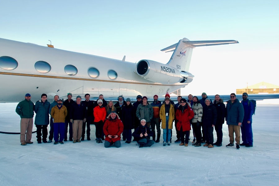 A group of individuals in winter clothing, standing on the ice in front of an airplane.