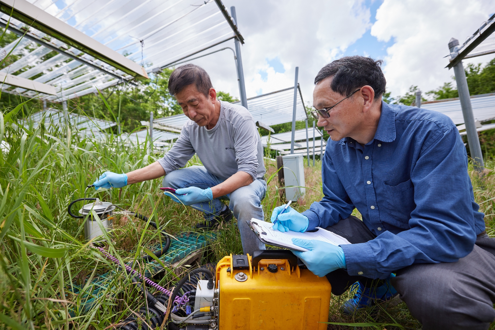 Two researchers crouching in a field of grass with scientific instruments. 
