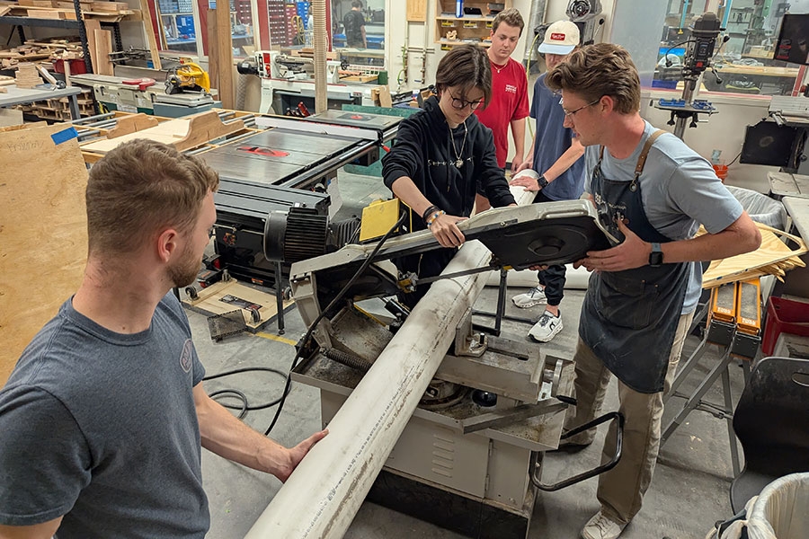 Several college students work with a large mechanical pipe and machinery in a laboratory.