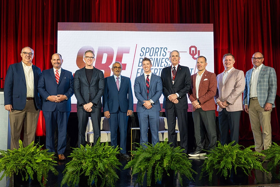 A group of men in suits stand together across a stage.