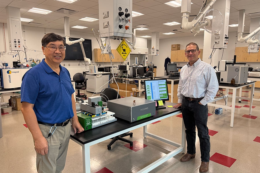 Two men stand next to a table inside a science laboratory.