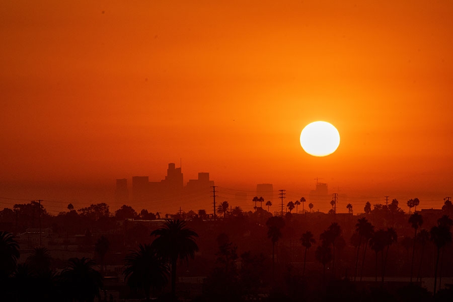 The sun in an orange sky over a city skyline.
