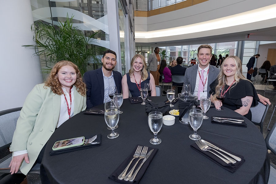 Five people sitting at a table with linens and silverware.