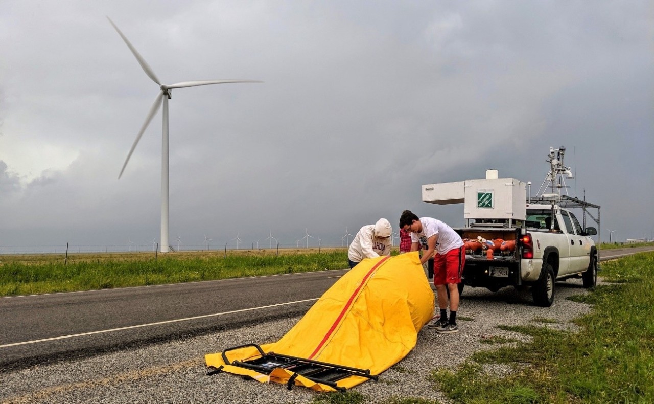 Two student researchers prepare a bright yellow balloon to carry radiosonde into the atmosphere to measure data from the storm brewing on the horizon.