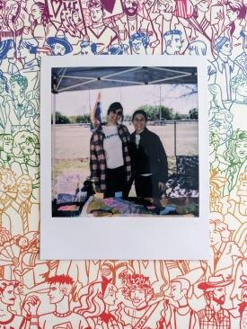 Polaroid photograph of two ciswomen, standing behind a table outside, smiling. Meghan Dudley, the project's manager, is on the left.